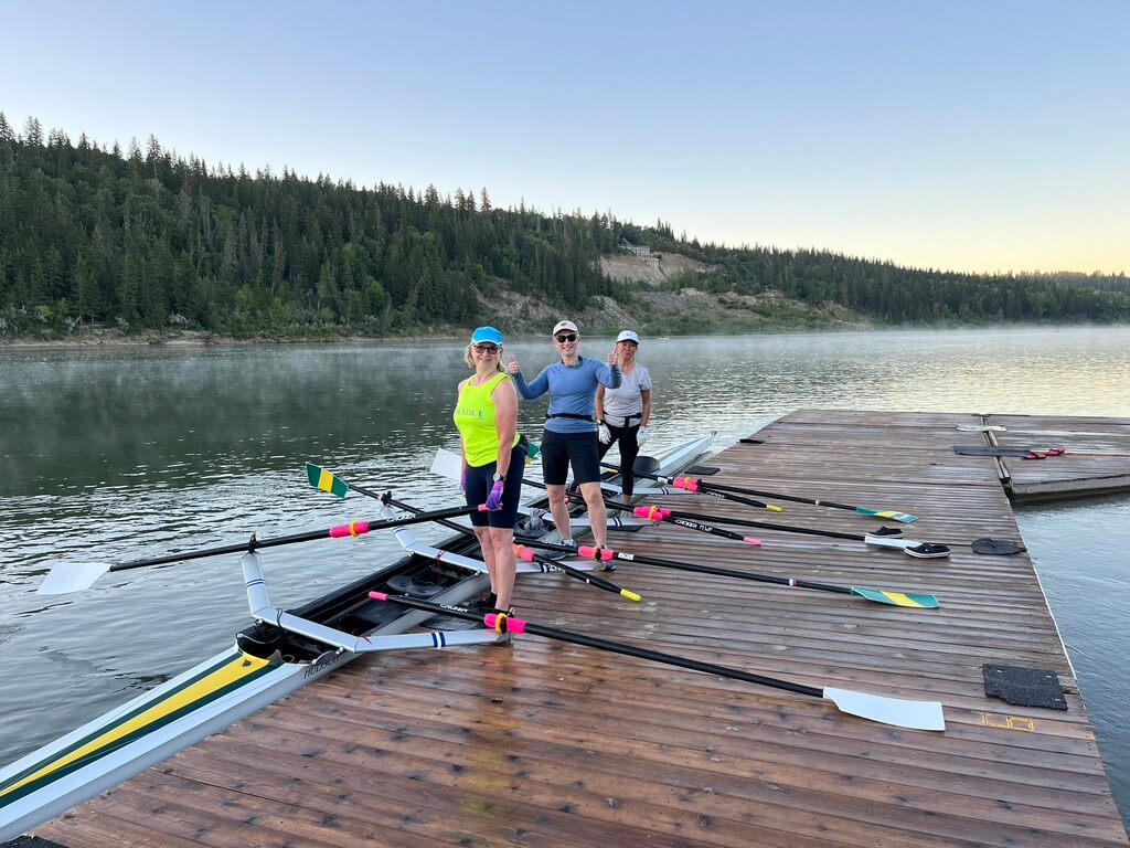 Rowers standing on the dock posing beside a quadruple rowing shell in the North Saskatchewan River