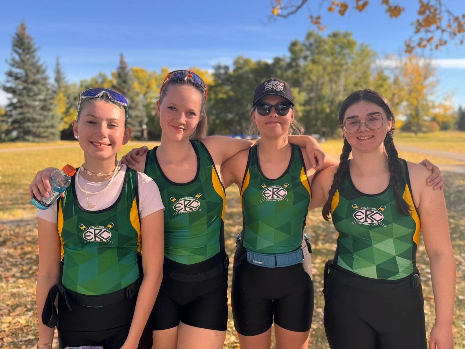Four female rowing athletes posting for a group photo set in a park with autumn leaves on the ground.
